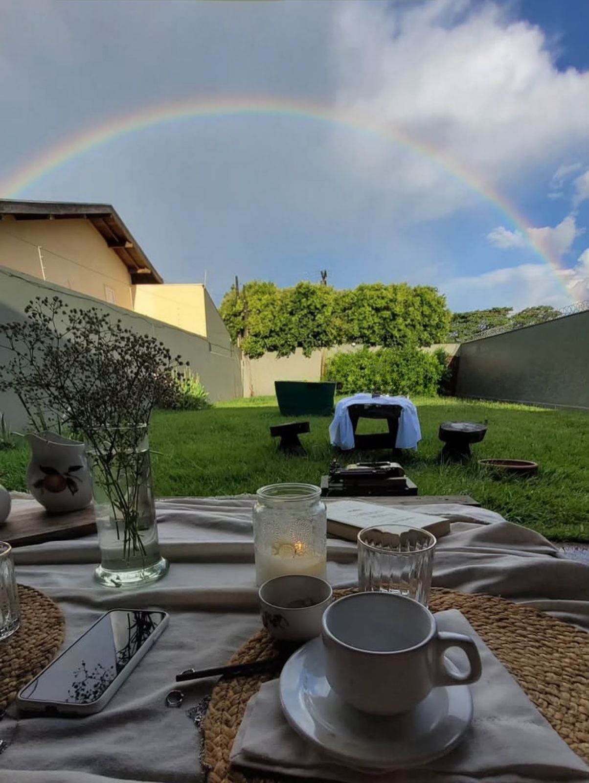 Vista do jardim da Casa Verde com arco-íris ao fundo e mesa de café da manhã